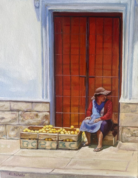 Woman sitting on a step with a crate of lemons in front of a wooden door.